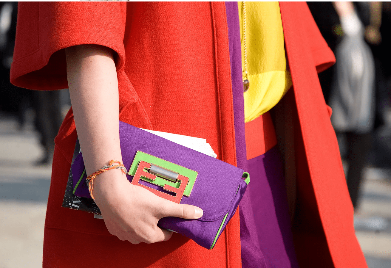 Image of the mid-section of a person on the street at the Colville Spring 21 show. We see a yellow top with a red jacket and purple handbag.