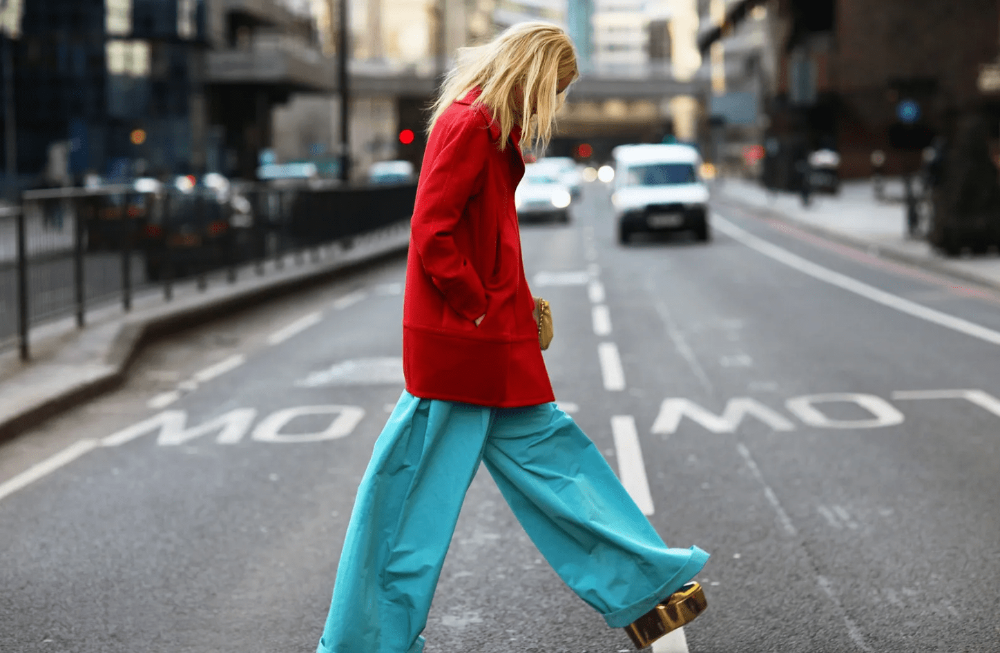 Person crossing the street at the Colville Spring 21 shows. They wear a red jacket with a cyan-like creamy blue trousers.