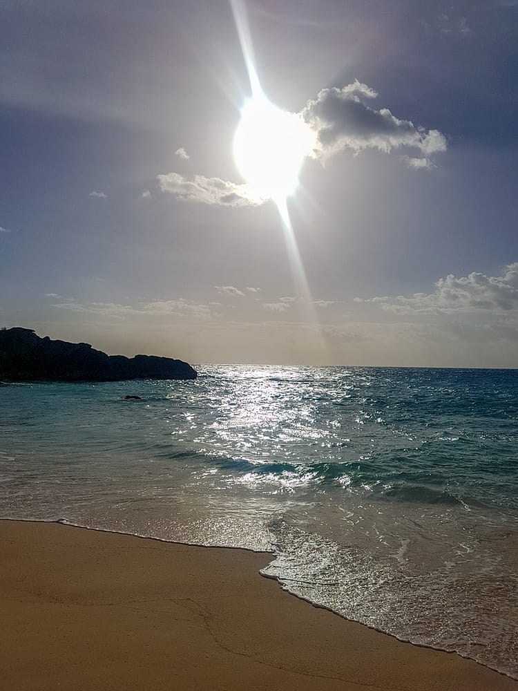 Bright sun glistening on the sea at sunset on a beach in Bermuda. Dark rocks in the distance which are emerging along the shoreline.