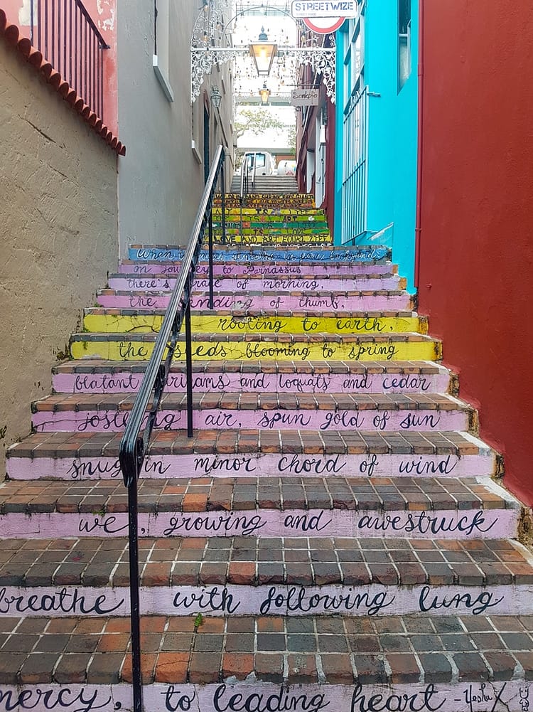 Colorful steps and rail on small side street in Bermuda with writing along each step.