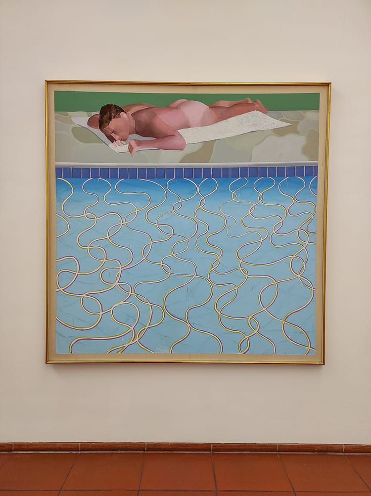 Painting of naked sunbather by pool where the pool takes up roughly 3/4 of the artwork. Painting by David Hockney called Sunbather. On display in Ludwig Museum.