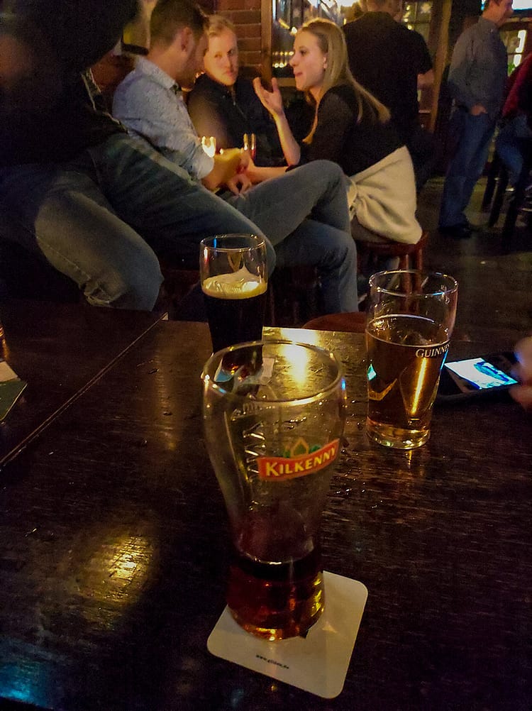 Three pints of Kilkenny and Guinness on a bar table in Barney, with people chatting in background, at Vallely's Irish pub, Cologne