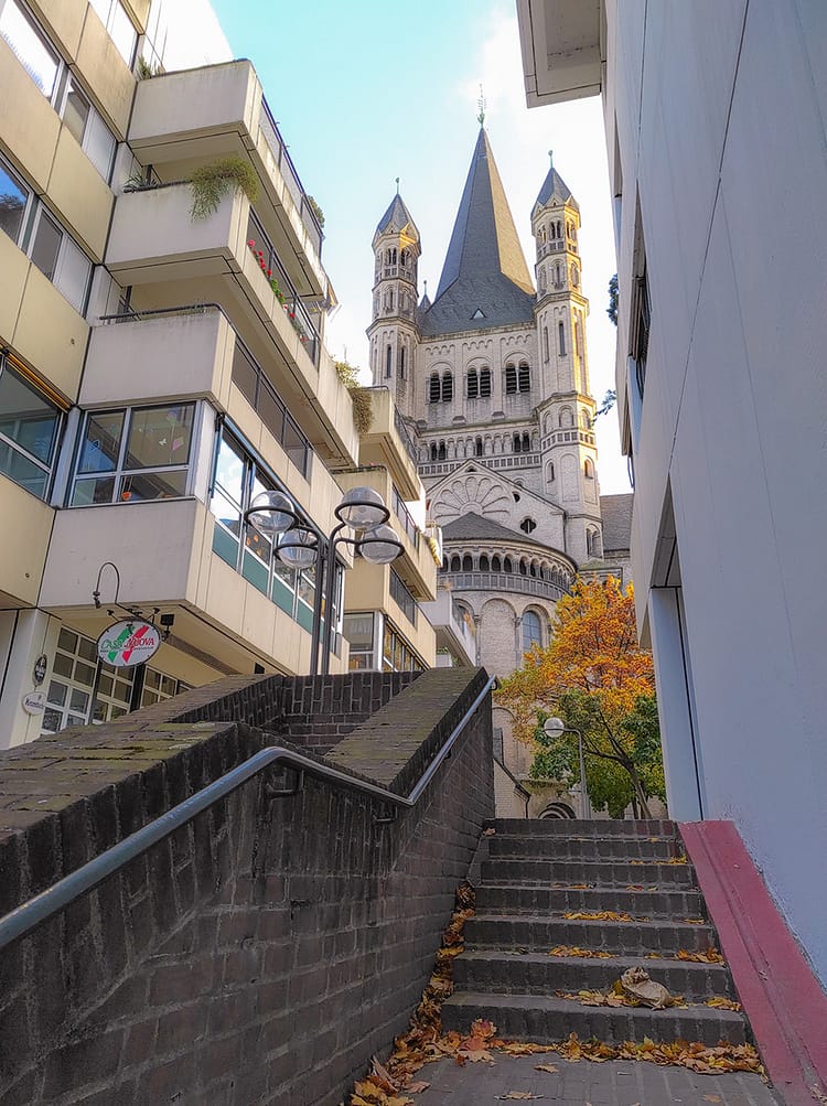 Steps upwards towards Groß St. Martin Church, in Cologne. Green and autumnal orange leaves on tree at top of steps.