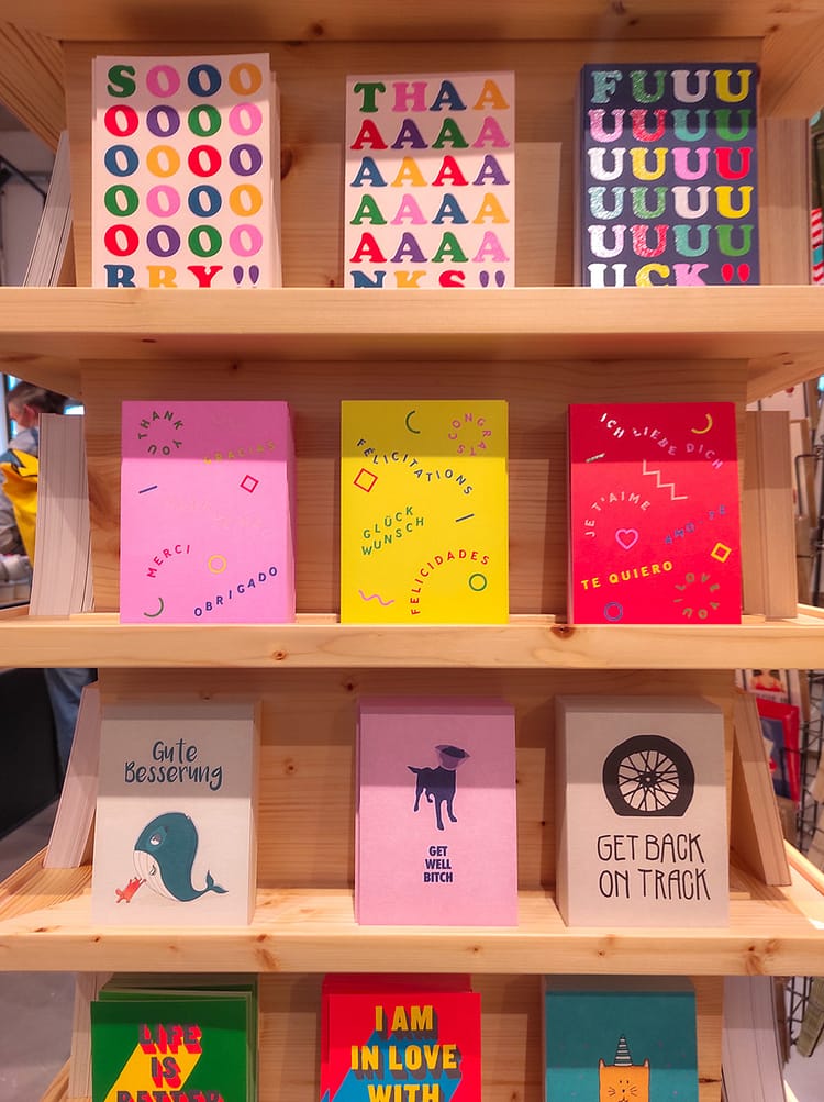 Three rows of colorful cards on a wooden stand for sale in Schee, Cologne.