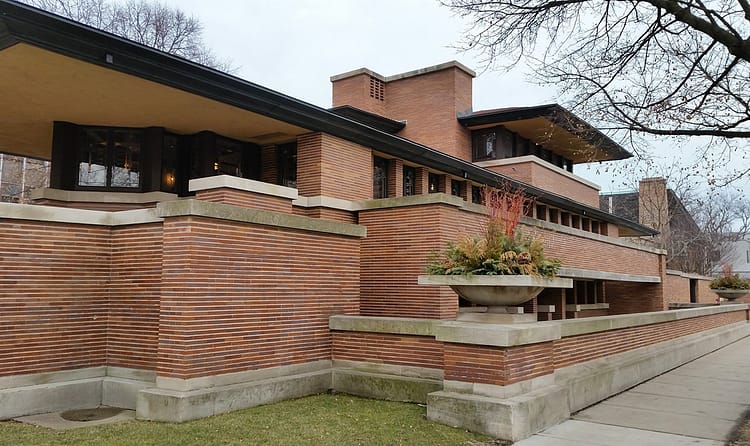 Prairie Style Architecture, Frank Lloyd Wright red brick building with grass and tree beside it. Building is in the style of the arts and crafts movement.