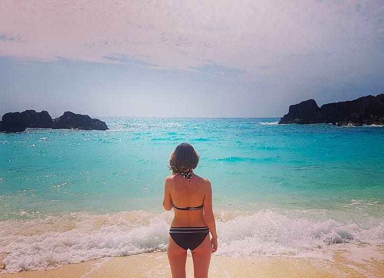Girl in bikini looking out over aqua blue sea at East Whale Beach, Bermuda. 