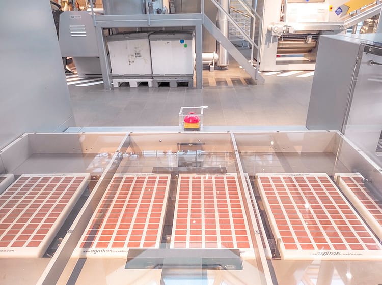 Rows and rows of rectangle milk chocolate in white containers on the machinery assembly line of the chocolate making process.