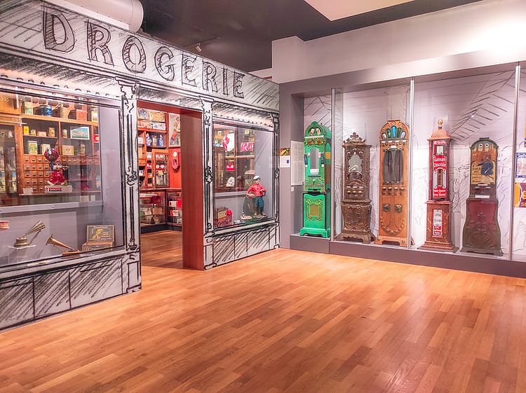 Indoor installation of a historic grey Drogerie (drug store) with artificacts and chocolate machines on display.