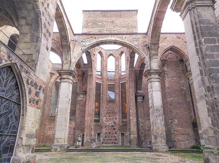 Ruins of the interior of an 11 Century Romanesque church. Large pillars stand as a facade which appears to frame where an altar was. Monument statues of grieving parents can be seen.