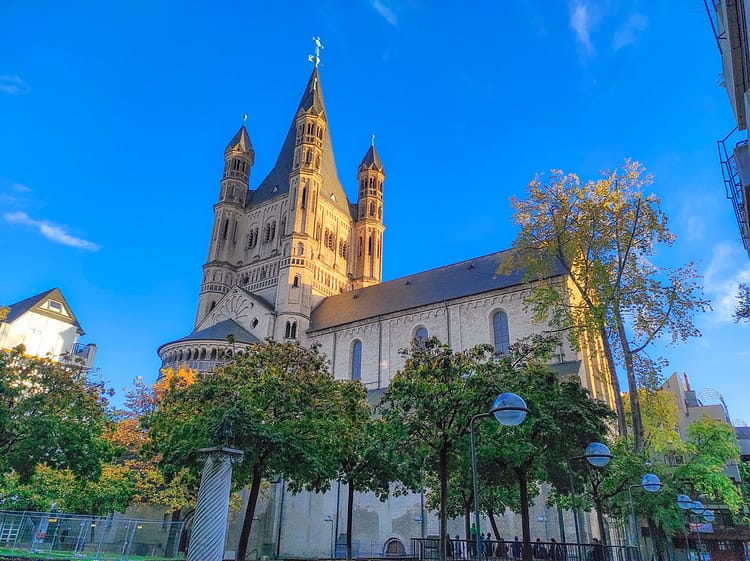 View of Groß St. Martin Church, in Cologne, surrounded by green trees and blue sky.