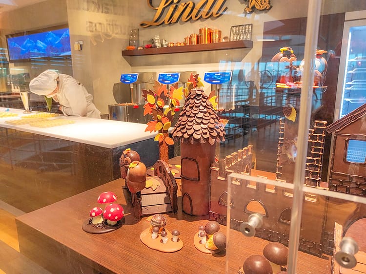Chocolate building and display with chocolate factory worker dressed in white at work in the background.