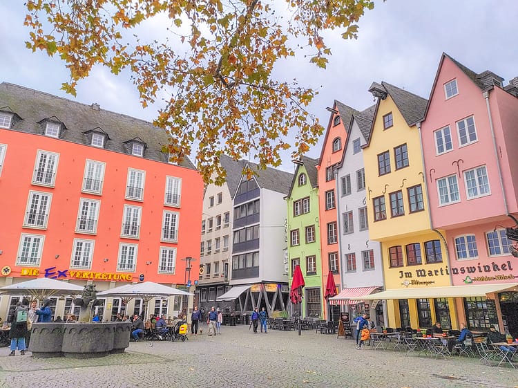 Colorful German architecture style buildings at Fishmarkt Square. Fountain in front of buildings in the center of the image. Cobblestone square in front of buildings where fountain is sitting.