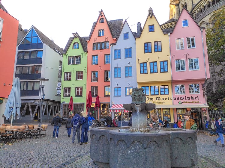 Colorful German architecture style buildings at Fishmarkt Square. Fountain in front of buildings in the center of the image. Cobblestone square in front of buildings where fountain is sitting.