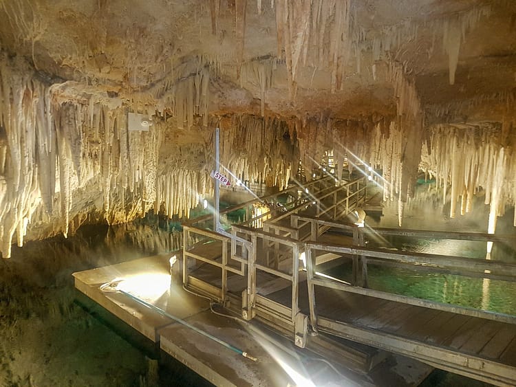 Wooden railway path over water walking through Crystal Cave, Bermuda, with hanging stalactites and stalagmites.
