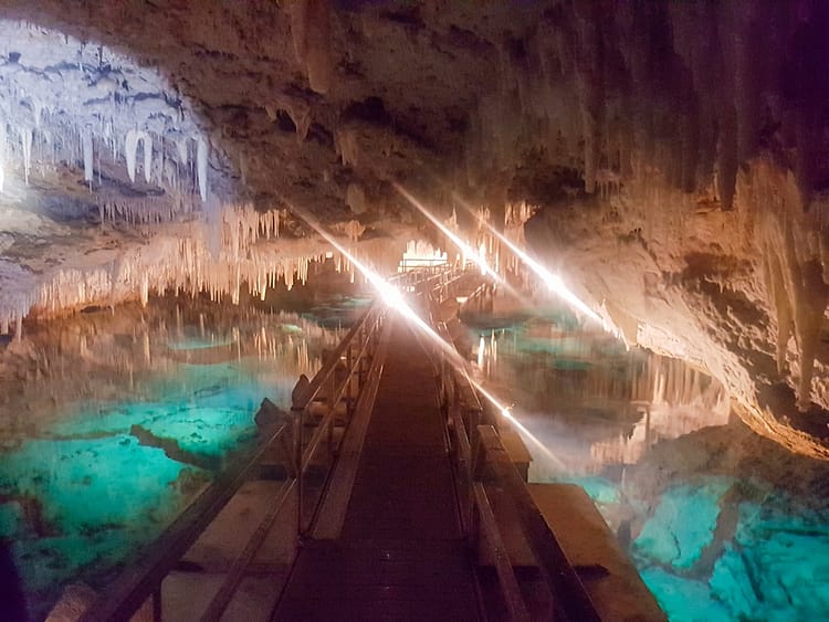 Wooden railway path over aqua blue water walking through Crystal Cave, Bermuda, with hanging stalactites and stalagmites.