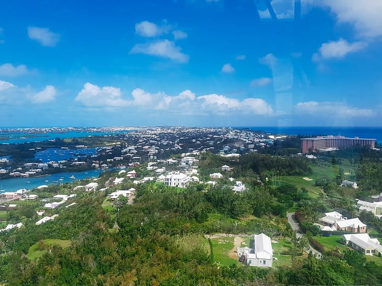 View overlooking Bermuda island from the top of Gibb's Hill Lighthouse. Greenery, rooftops, blue sea, boats, and Fairmont Hotel.