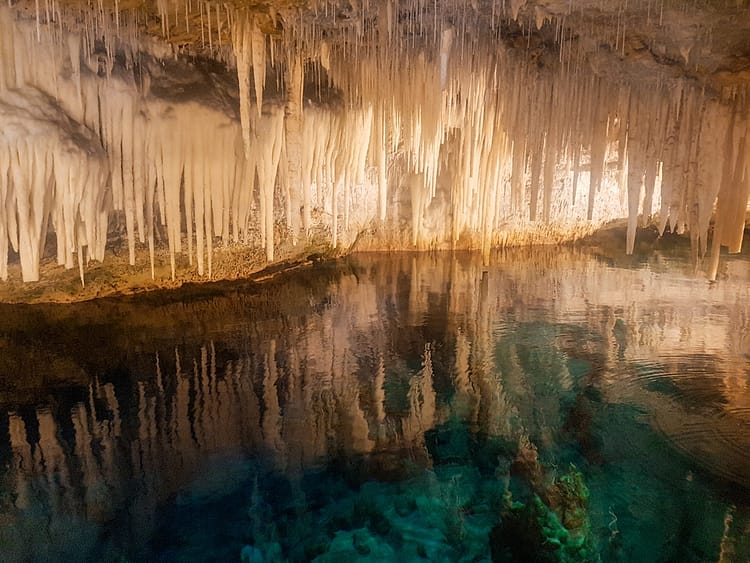 Hanging stalactites and stalagmites, over aqua blue water, in Crystal Cave, Bermuda.