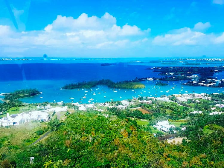 View overlooking Bermuda island from the top of Gibb's Hill Lighthouse. Greenery, rooftops, blue sea, white boats.