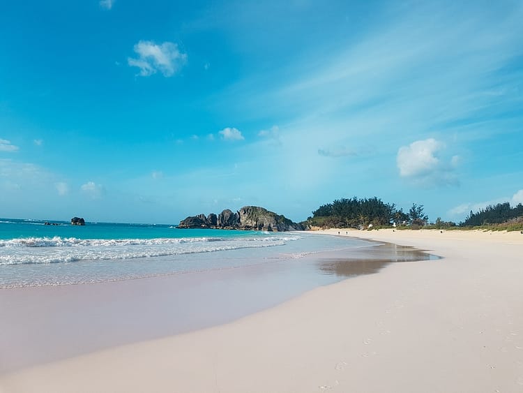 Blue sky, sand, sea, some greenery and rocks in the distance at Horseshoe Bay, Bermuda.