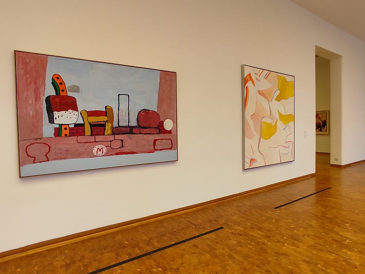 Two colorful artworks on a white wall with brown wood floor in Ludwig Museum