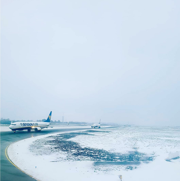 Two Ryanair planes on the runway at Dublin Airport, surrounded by snow.