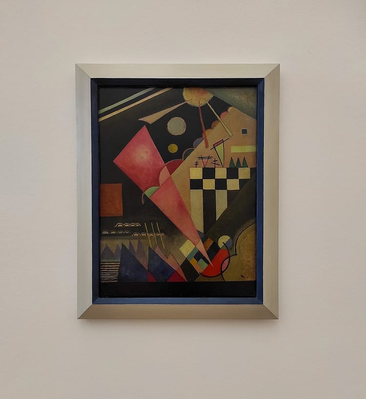 Variety of shapes , in different colors, within artwork by Wassily Kandinsky on display in Ludwig Museum. Main central shape is a pinky red triangle towards the center of the piece. Artwork called Scharfruhiges Rosa.