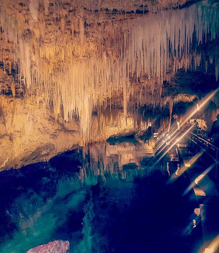 Hanging stalactites and stalagmites, over aqua blue water, in Crystal Cave, Bermuda.