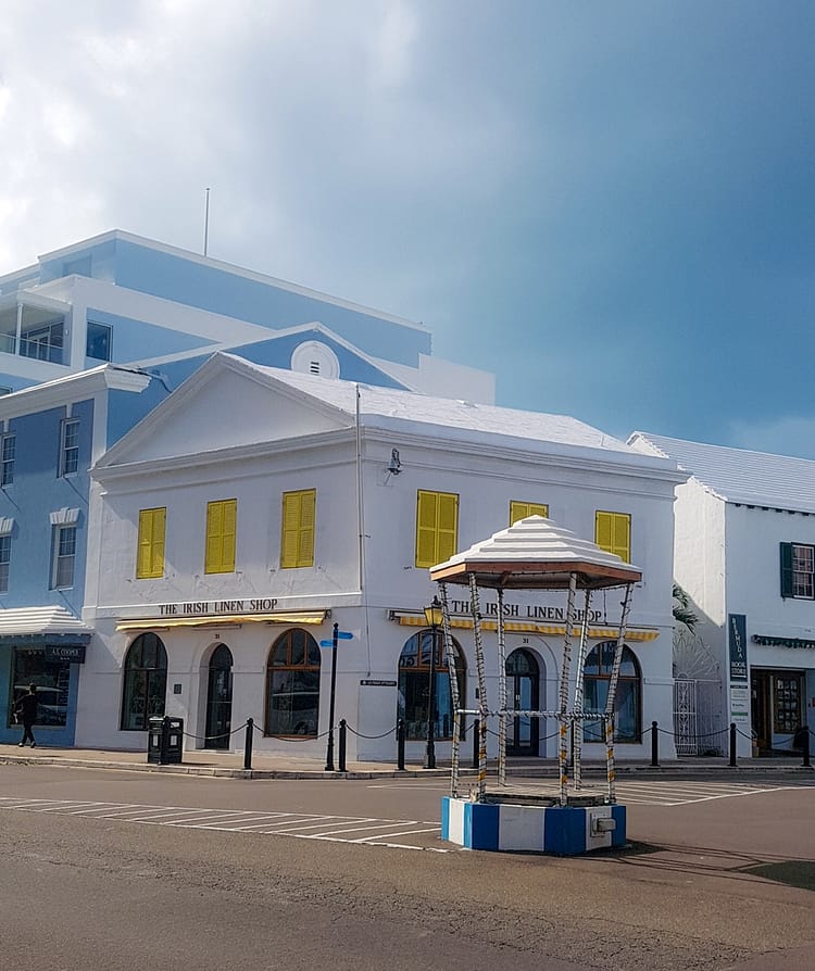 Crossroads on Front Street with white building, and yellow shutter frames, stating "The Irish Linen Shop" on Front Street, Bermuda.