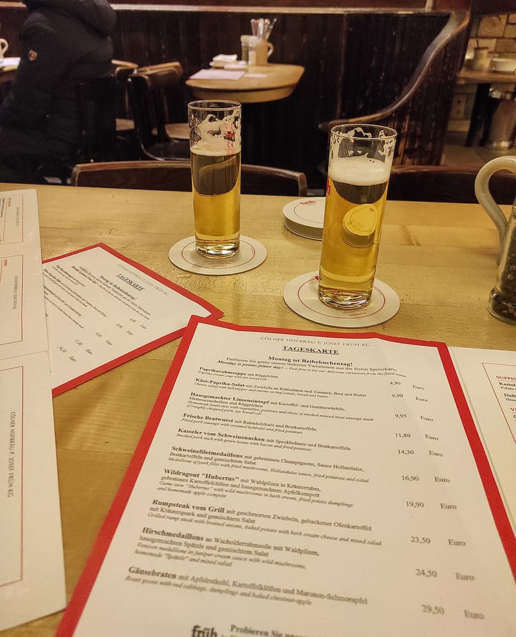 Wooden table in Brauhaus Früh am Dom, Cologne, with two beers and menus on it.