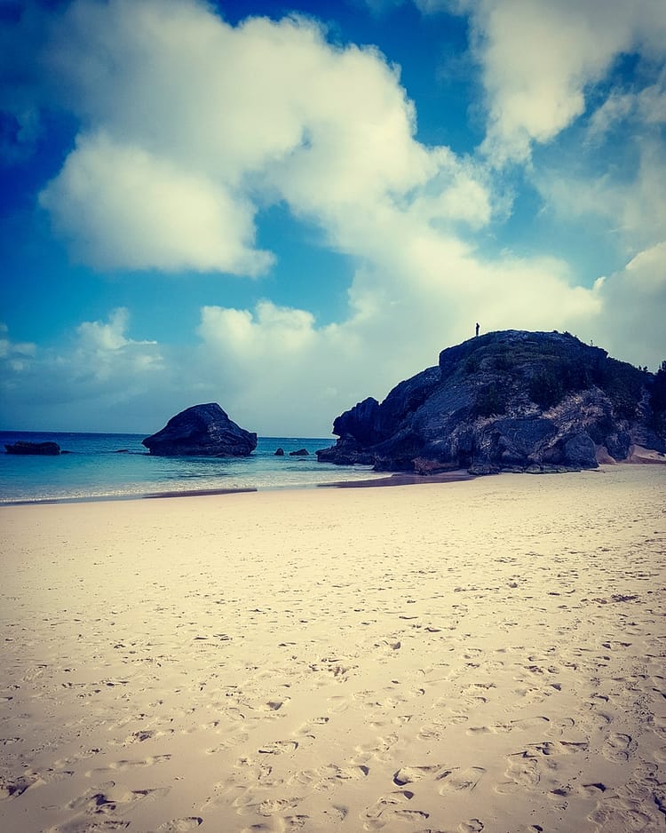 Looking out over the sand to the sea, with a person standing on top of rocks, at Horseshoe Bay, Bermuda, beach.