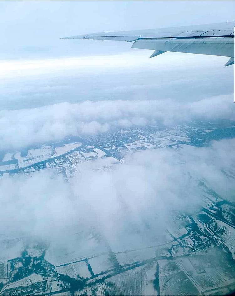 View from the sky through an aeroplane window overlooking white clouds and fields covered in snow in Ireland.